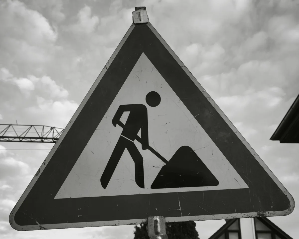 Baustellenschild vor bewölktem Himmel Schwarzweißfoto eines Baustellenschilds mit Arbeiter-Piktogramm vor bewölktem Himmel