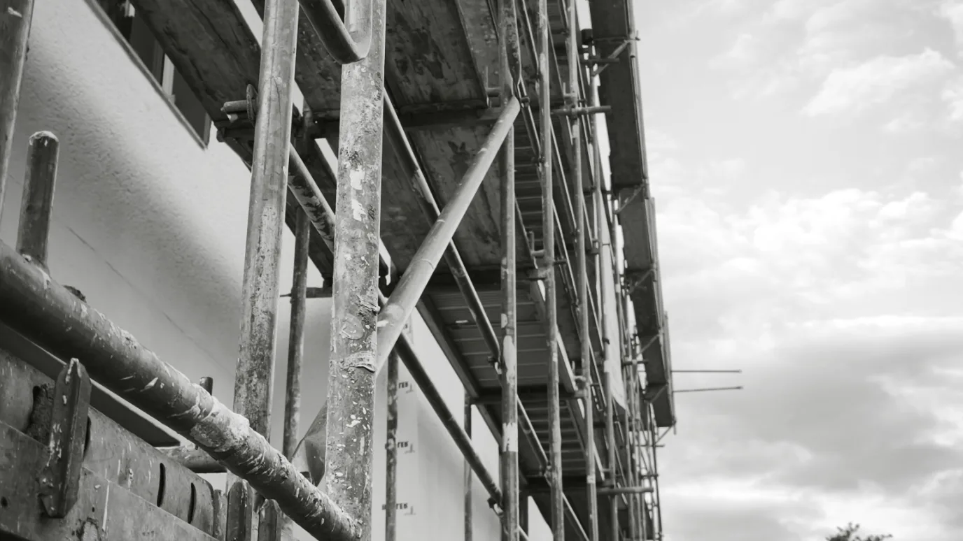 Typische Fehler auf Handwerker-Websites: Gerüst an einer Baustelle Schwarzweißfoto eines Baustellengerüsts an einer Hausfassade vor bewölktem Himmel